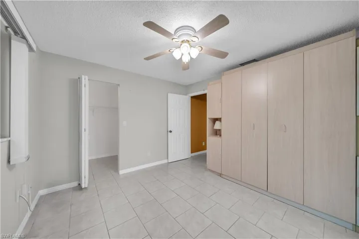 Unfurnished bedroom with a walk in closet, light tile patterned flooring, a textured ceiling, and a ceiling fan