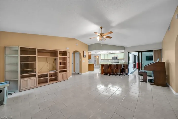 Living room with vaulted ceiling, light tile patterned floors, ceiling fan, and arched walkways