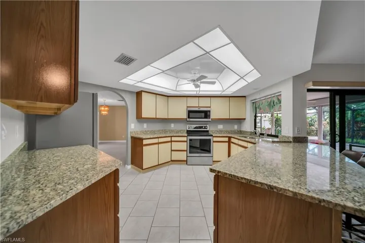 Kitchen featuring stainless steel appliances, arched walkways, a kitchen breakfast bar, light stone counters, and ceiling fan