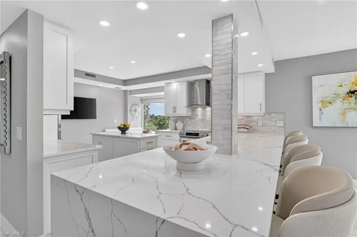 Kitchen featuring a peninsula, a center island, white cabinetry, light stone countertops, and a breakfast bar