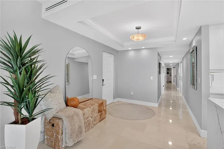 Hallway with arched walkways, recessed lighting, a raised ceiling, and ornamental molding