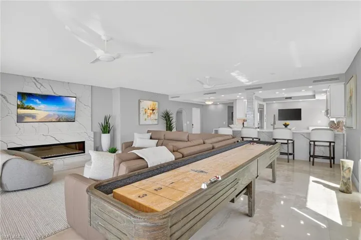 Living room with ceiling fan, a fireplace, light marble finish flooring, and decorative columns