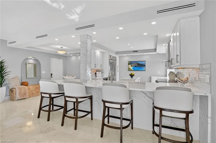 Kitchen featuring white cabinets, light stone countertops, tasteful backsplash, a peninsula, and a raised ceiling