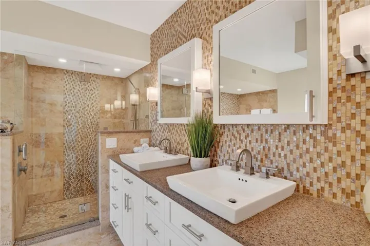 Bathroom featuring double vanity, a tile shower, backsplash, and tile walls