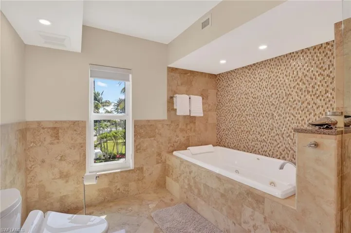 Bathroom featuring tile walls, a jetted tub, recessed lighting, and wainscoting