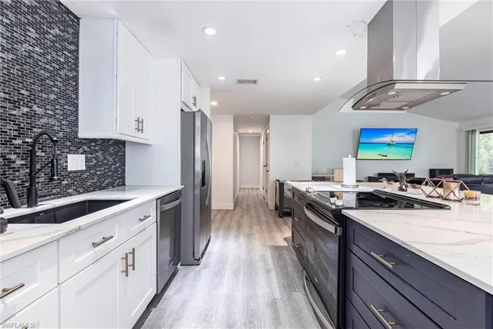 Kitchen with stainless steel appliances, island range hood, open floor plan, white cabinets, and light stone counters