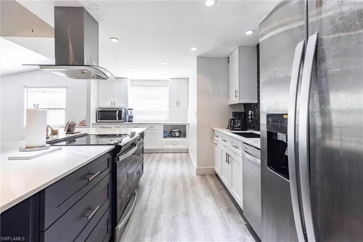 Kitchen featuring appliances with stainless steel finishes, island exhaust hood, white cabinetry, light countertops, and light wood-style floors