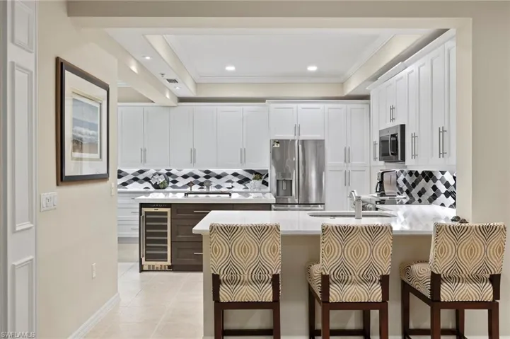 Kitchen with appliances with stainless steel finishes, decorative backsplash, white cabinetry, a tray ceiling, and wine cooler