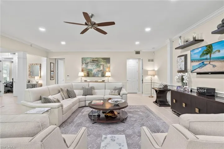 Tiled living room with ornate columns, ceiling fan, and crown molding