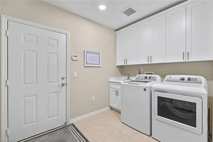 Laundry area featuring separate washer and dryer, cabinets, light tile patterned floors, and sink