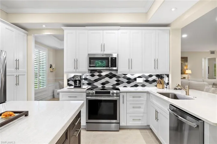 Kitchen featuring light tile patterned flooring, white cabinets, ornamental molding, appliances with stainless steel finishes, and backsplash