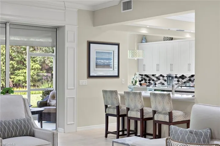 Kitchen with decorative backsplash, white cabinetry, a kitchen breakfast bar, and ornamental molding
