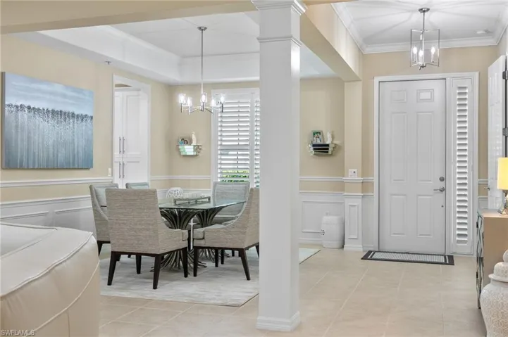 Dining area featuring ornate columns, an inviting chandelier, light tile patterned floors, and crown molding