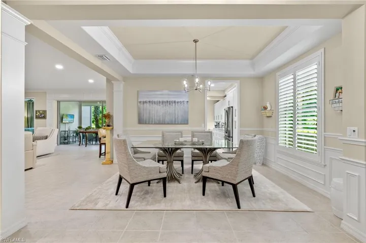 Tiled dining area with a notable chandelier, ornamental molding, and a tray ceiling