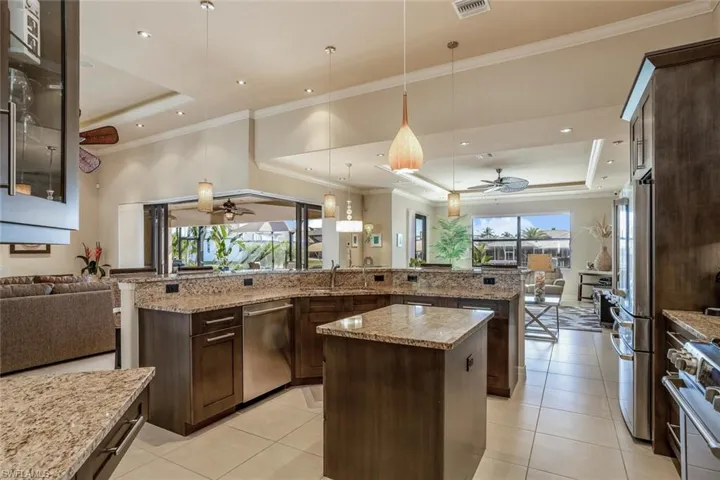 Kitchen featuring open floor plan, a raised ceiling, dark brown cabinetry, light stone counters, and crown molding