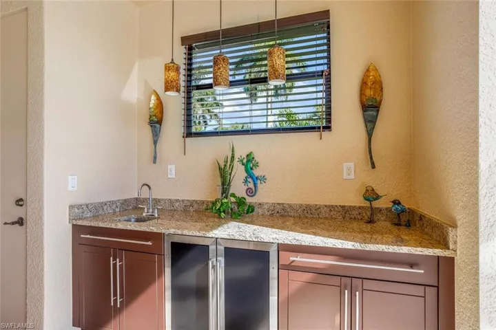 Indoor wet bar featuring a textured wall, light stone countertops, stainless steel refrigerator, and wine cooler