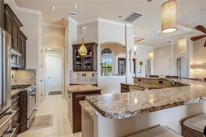 Kitchen with arched walkways, glass insert cabinets, dark brown cabinets, a kitchen breakfast bar, and crown molding