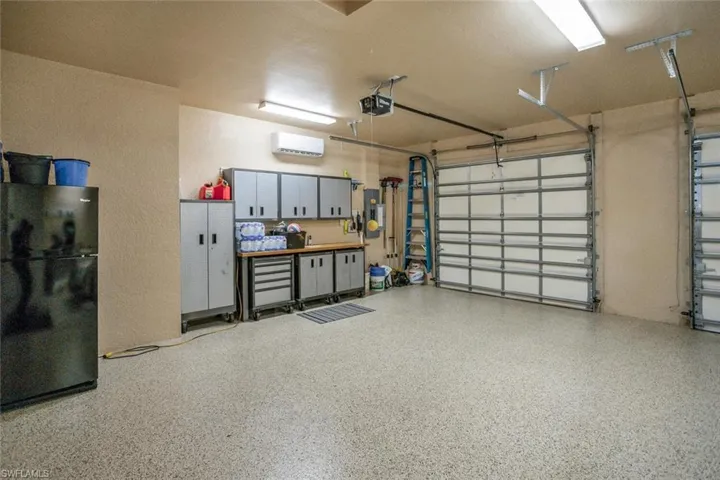 Garage with freestanding refrigerator, a wall unit AC, a garage door opener, and a textured wall