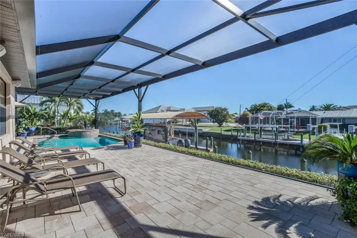 View of pool with a patio, a water view, a pool with connected hot tub, glass enclosure, and a dock