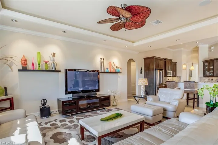 Living area with arched walkways, crown molding, a raised ceiling, and ceiling fan