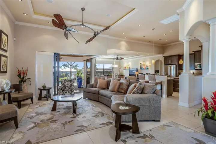 Living room with arched walkways, a ceiling fan, light tile patterned flooring, a towering ceiling, and a raised ceiling