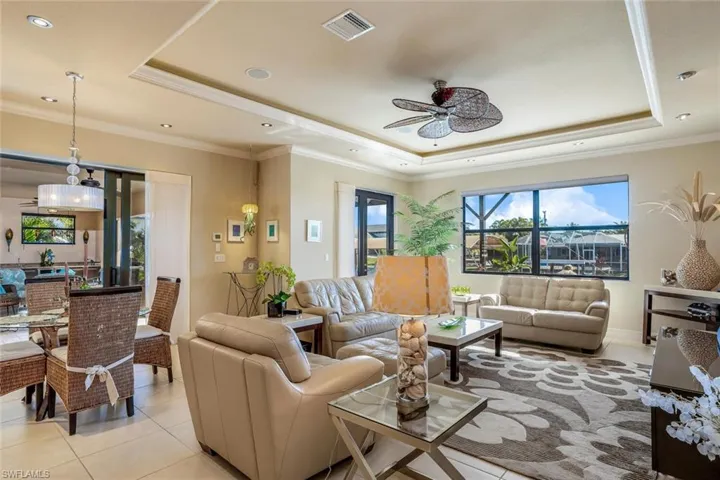 Living area with a ceiling fan, crown molding, a tray ceiling, and light tile patterned floors