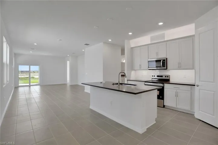 Kitchen featuring stainless steel appliances, dark countertops, a kitchen island with sink, white cabinetry, and recessed lighting