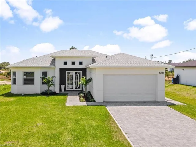 Prairie-style house featuring french doors, a front lawn, driveway, a garage, and stucco siding