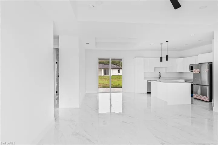 Open-concept kitchen featuring white cabinetry, center island with quartz countertop, stainless steel appliances, recessed ceiling, and polished tile flooring