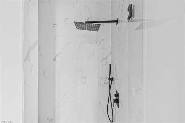 Shower featuring floor-to-ceiling stone-finish tile, matte black wall-mounted rainfall shower head, and matching handheld shower fixture