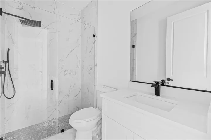 Walk-in shower with floor-to-ceiling stone-patterned tile, glass enclosure, and rainfall showerhead, complemented by a white vanity with integrated basin and matte black fixtures