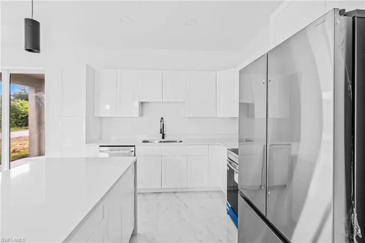 Kitchen featuring high-gloss white cabinetry, white stone-finish countertops, stainless steel appliances, a high-arc faucet, and light-toned tile flooring