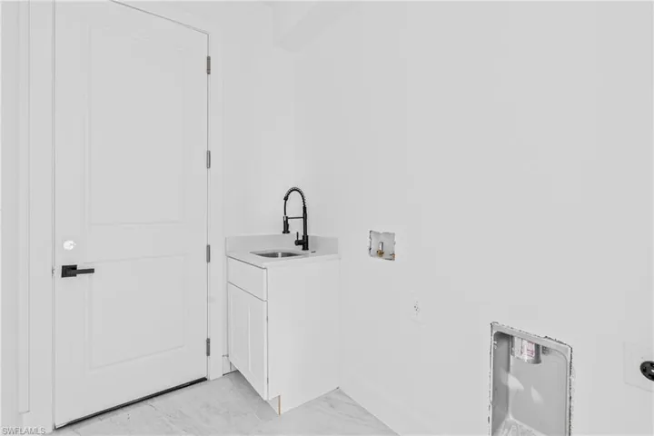 Utility area featuring a white shaker-style base cabinet, stone-composite countertop, matte black gooseneck faucet, drop-in basin, and tile flooring