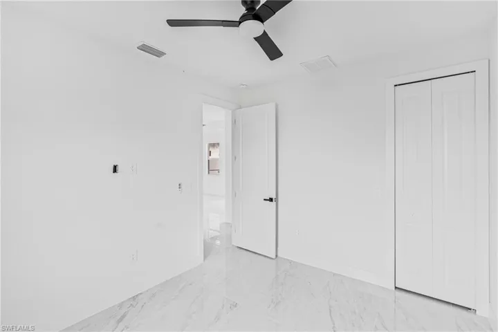 Neutral-toned interior space featuring stone-finish flooring, a matte black ceiling fan, and a closet with bifold doors