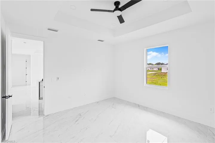 Room featuring tray ceiling, recessed lighting, matte black ceiling fan, stone-patterned tile flooring, and a single-pane window