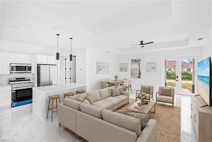 Open-concept interior featuring high tray ceilings, polished stone-finish tile flooring, a kitchen island with stone countertop, and glass-paned double doors