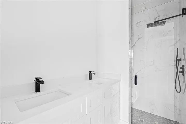 Double vanity featuring quartz countertops, integrated rectangular sinks, matte black widespread faucets, and a walk-in shower with floor-to-ceiling stone-look wall tile, matte black rainfall showerhead, and handheld sprayer