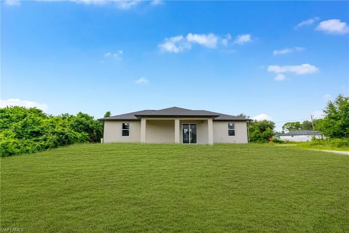 Stucco exterior featuring a covered patio, hipped roof, and expansive lawn