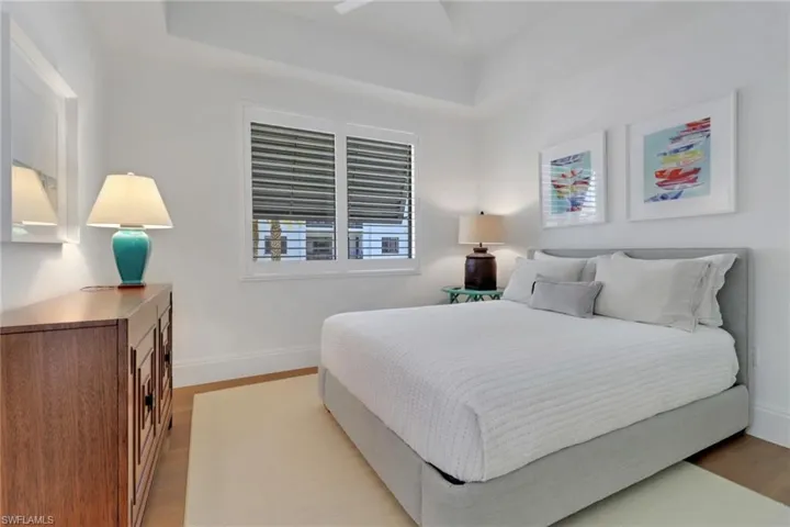 Guest bedroom with wood floors, plantation shutters, baseboards, fan & a tray ceiling