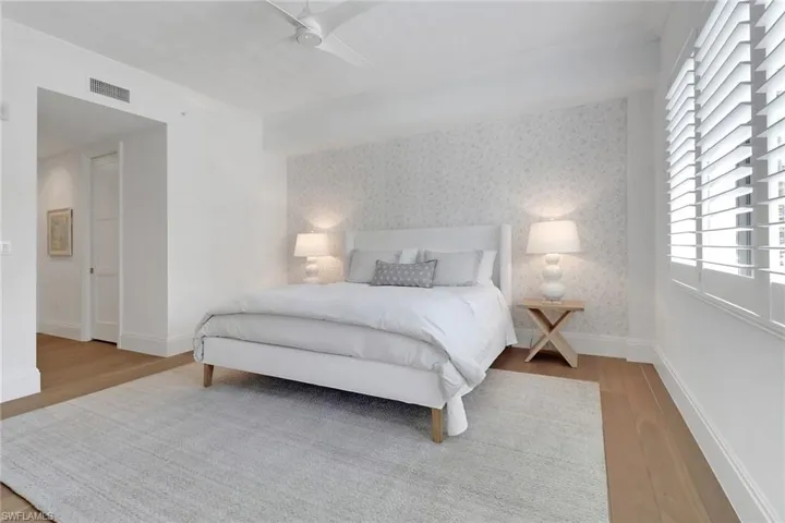 Large primary bedroom with plantation shutters, wood floors and wallpaper