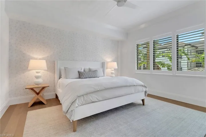 Large primary bedroom featuring wood floors, plantation shutters and Serena & Lily wallpaper