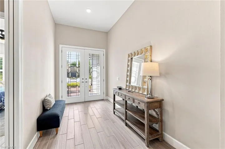 Double entry doors with decorative glass panels, recessed ceiling lighting, wood-look plank tile  flooring, and neutral wall tones throughout