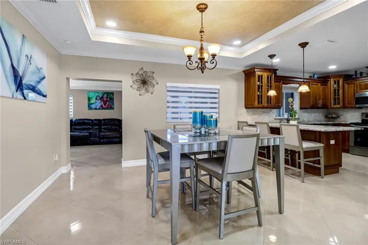 Dining room featuring light tile floors, a chandelier, a raised ceiling, and crown molding