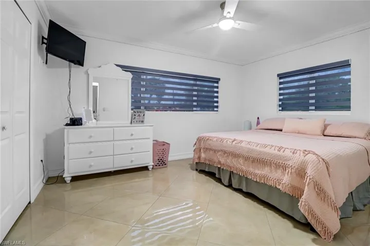 Bedroom with ceiling fan, crown molding, and light tile floors