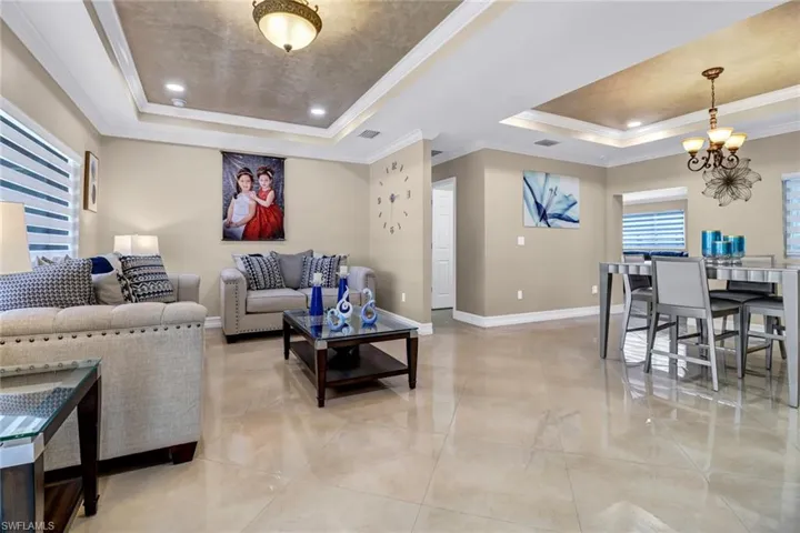 Tiled living room with crown molding, a tray ceiling, and an inviting chandelier