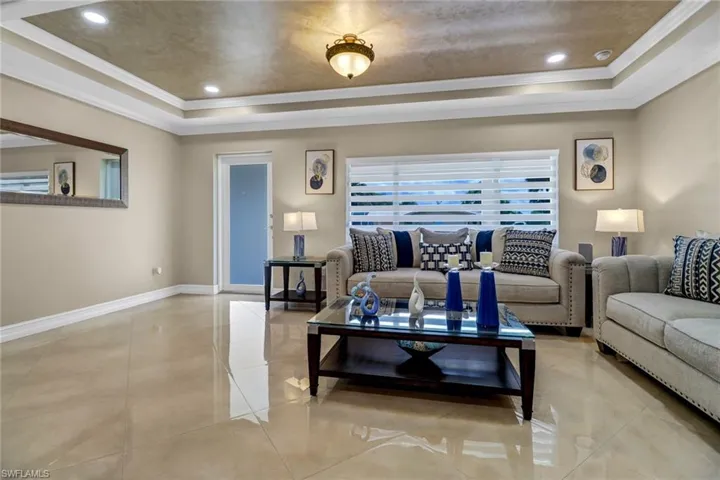 Tiled living room with crown molding and a raised ceiling