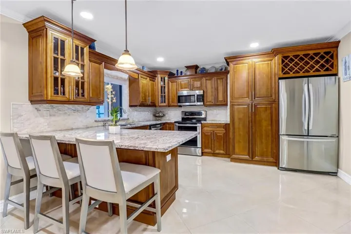 Kitchen with kitchen bar, light tile floors, tasteful backsplash, granite countertop, and stainless-steel appliances