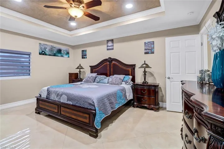 Bedroom featuring light tile floors, ornamental molding, ceiling fan, and a raised ceiling