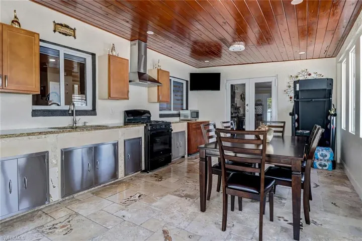 enclosed Lanai with an outdoor kitchen for gathering with a split AC system, travertine tile and a beautiful tongue and groove wood ceiling.