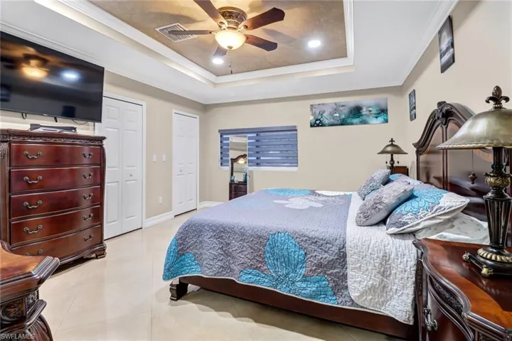 Tiled Master bedroom featuring a raised ceiling, ceiling fan, and crown molding